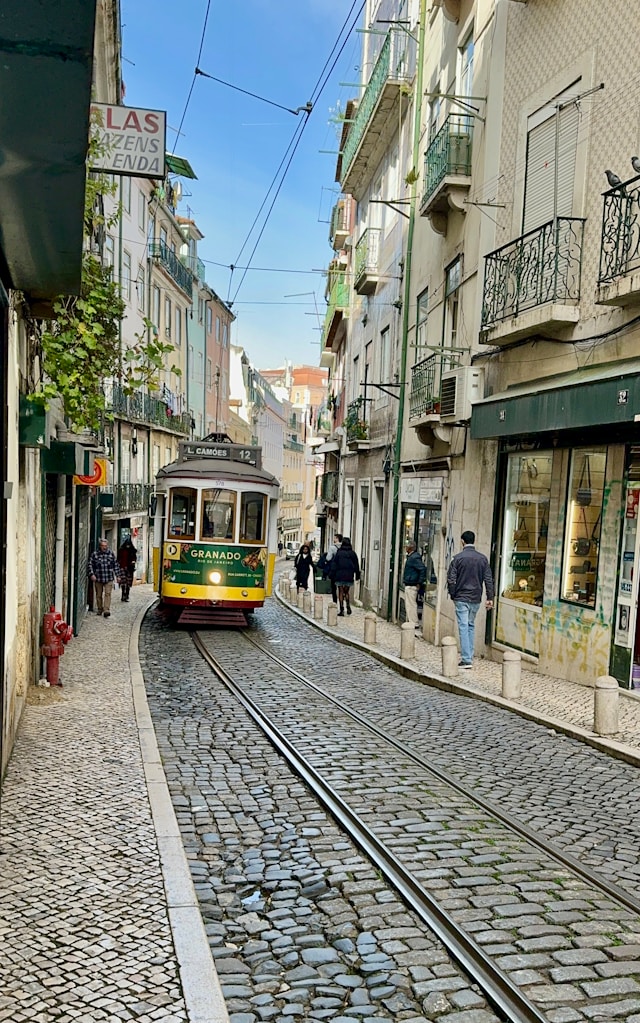 A historic yellow tram on a cobblestone street in Lisbon, Portugal.